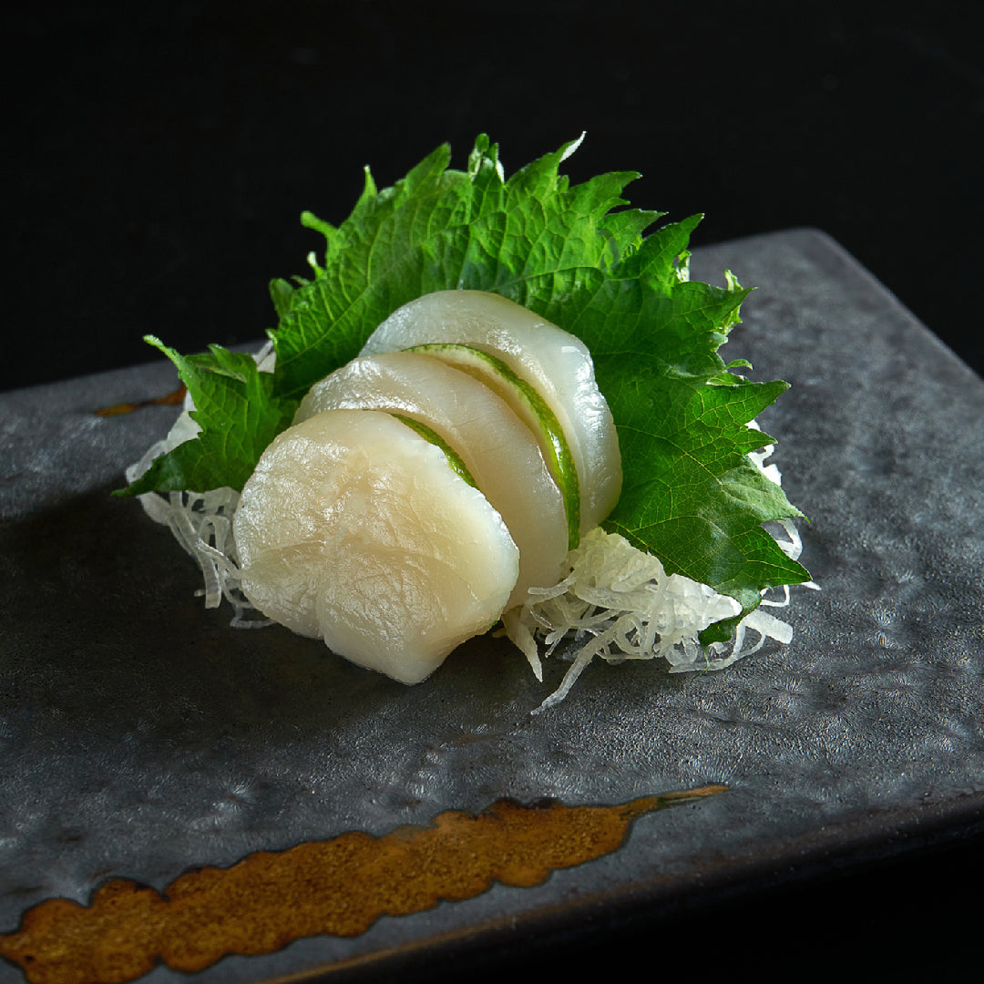 Live scallops in the shell stored on a bed of crushed ice in a shallow tray, showing proper storage technique to maintain freshness and temperature