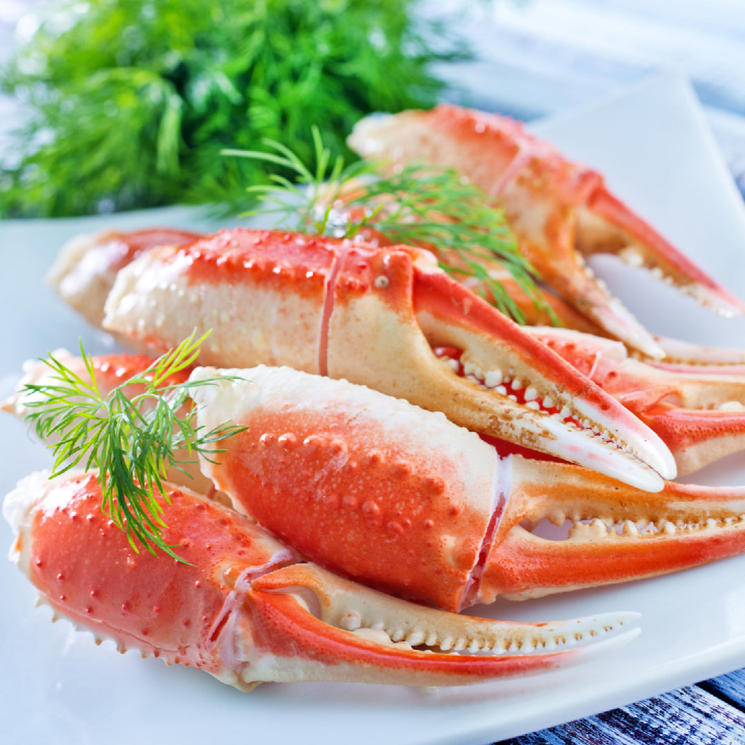 Snow crab legs being cracked open with kitchen scissors to extract sweet white crab meat, served with garlic butter and lemon