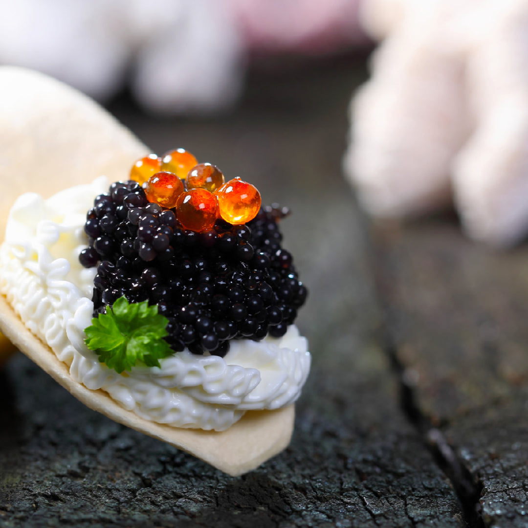 Osetra caviar spooned over salmon nigiri sushi on a slate board with a mother-of-pearl spoon and champagne