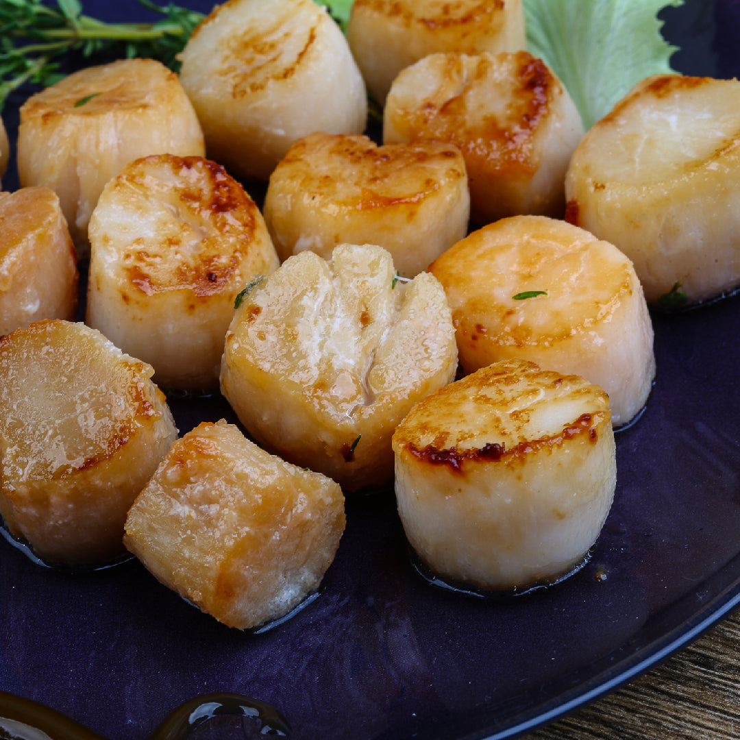 Seared diver scallops on a white plate alongside a chilled glass of Chardonnay