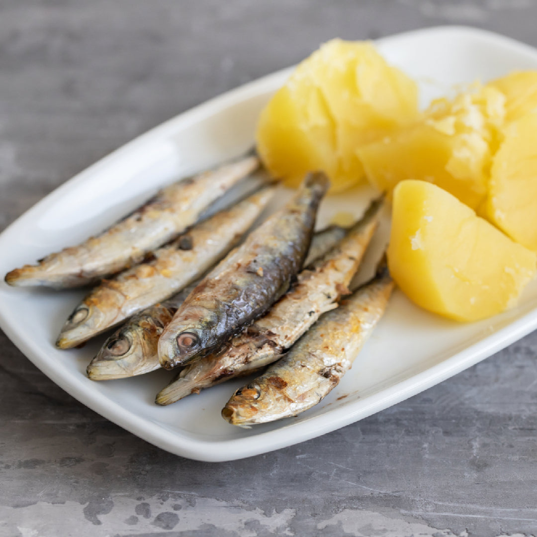 Rustic bowl of sardine tapenade with black olives, capers, and fresh parsley served alongside toasted baguette slices and a glass of white wine