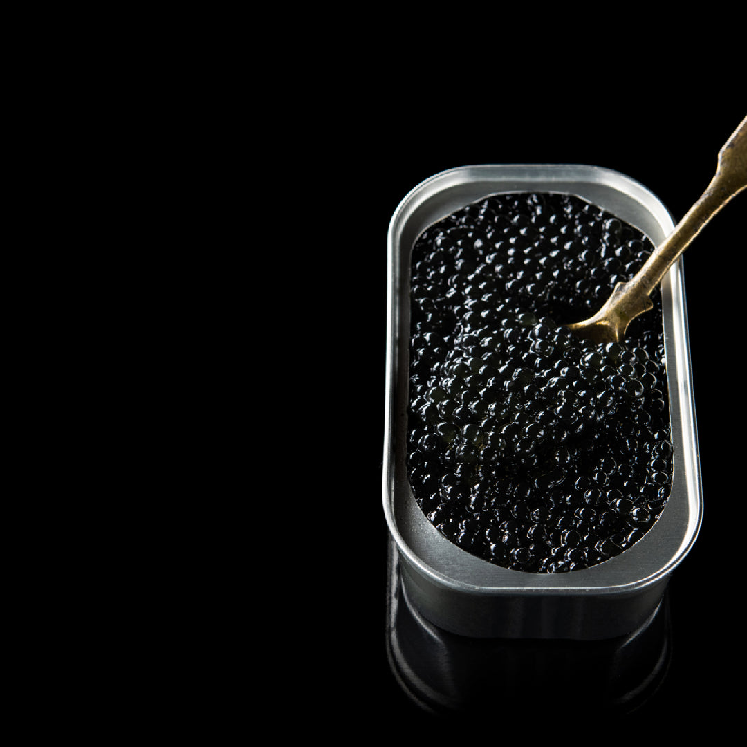 Sturgeon caviar tin open on a bed of crushed ice with a mother-of-pearl spoon and blinis alongside on a marble surface