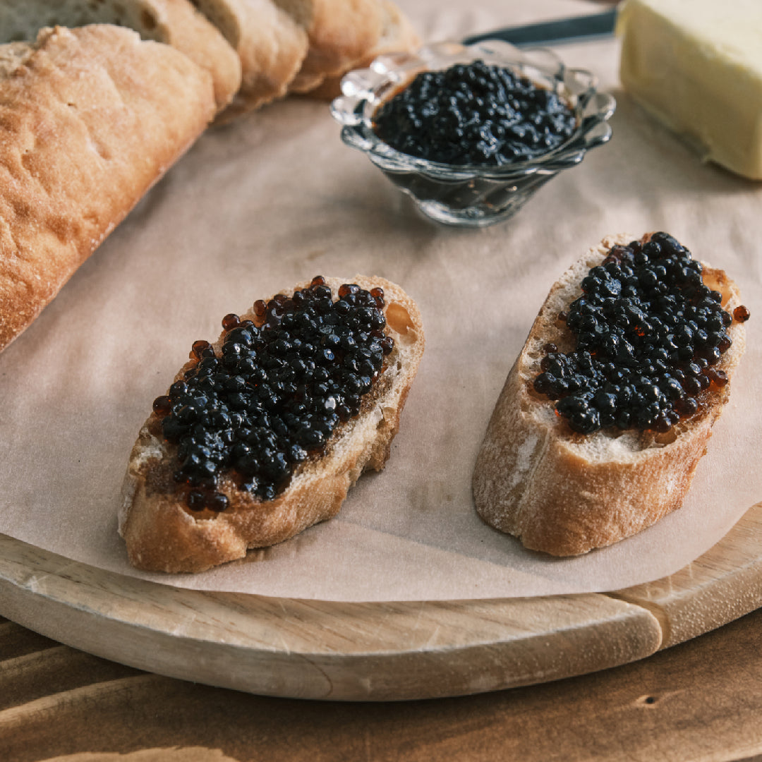 Tin of premium black sturgeon caviar pearls with a mother-of-pearl spoon on a dark background