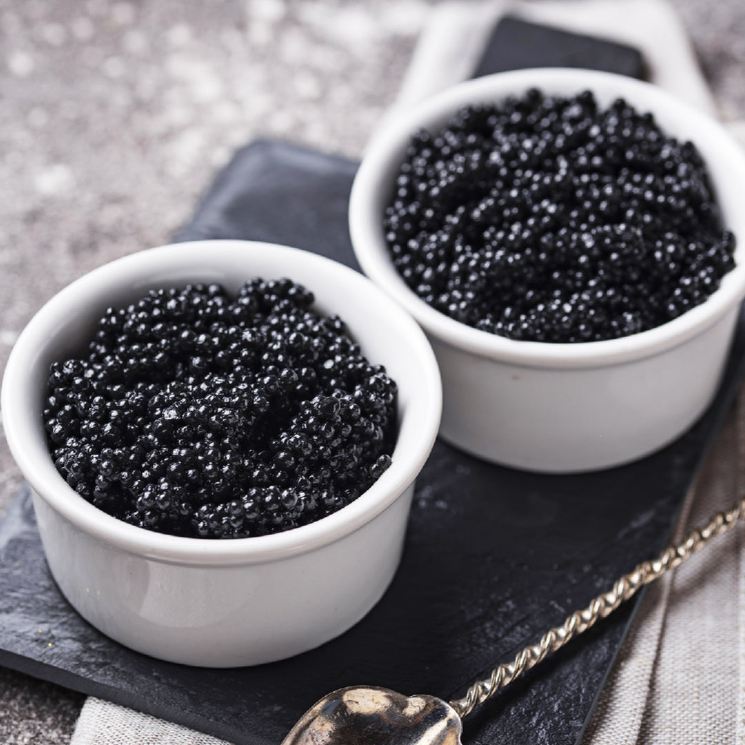 Elegant sturgeon caviar served on blinis with crème fraîche and a mother-of-pearl spoon on a white marble surface
