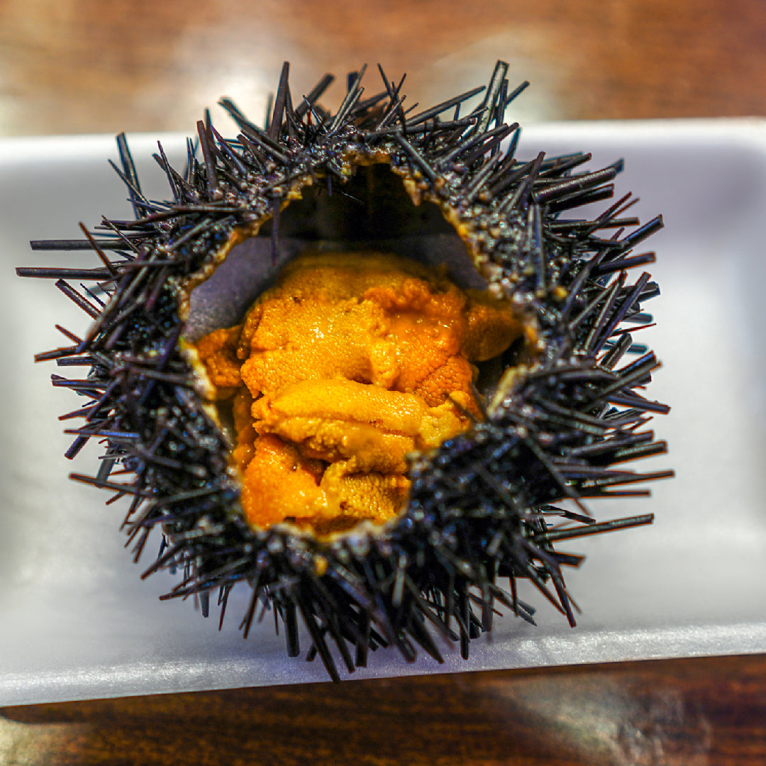 Freshly made sea urchin nigiri sushi with golden uni on seasoned rice, served on a wooden board with soy sauce and wasabi