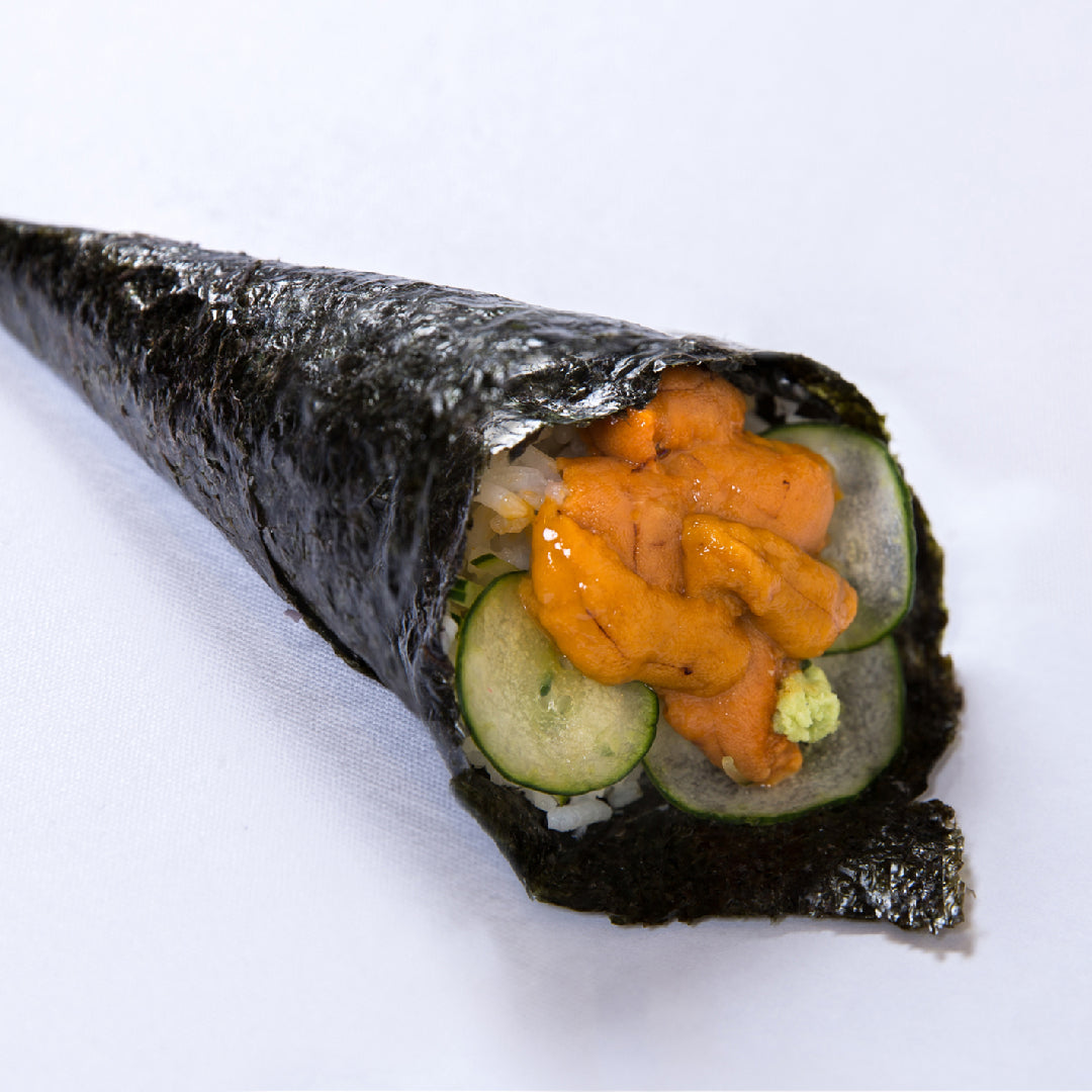Bright orange uni sea urchin roe pieces arranged on a wooden board next to a whole sea urchin shell