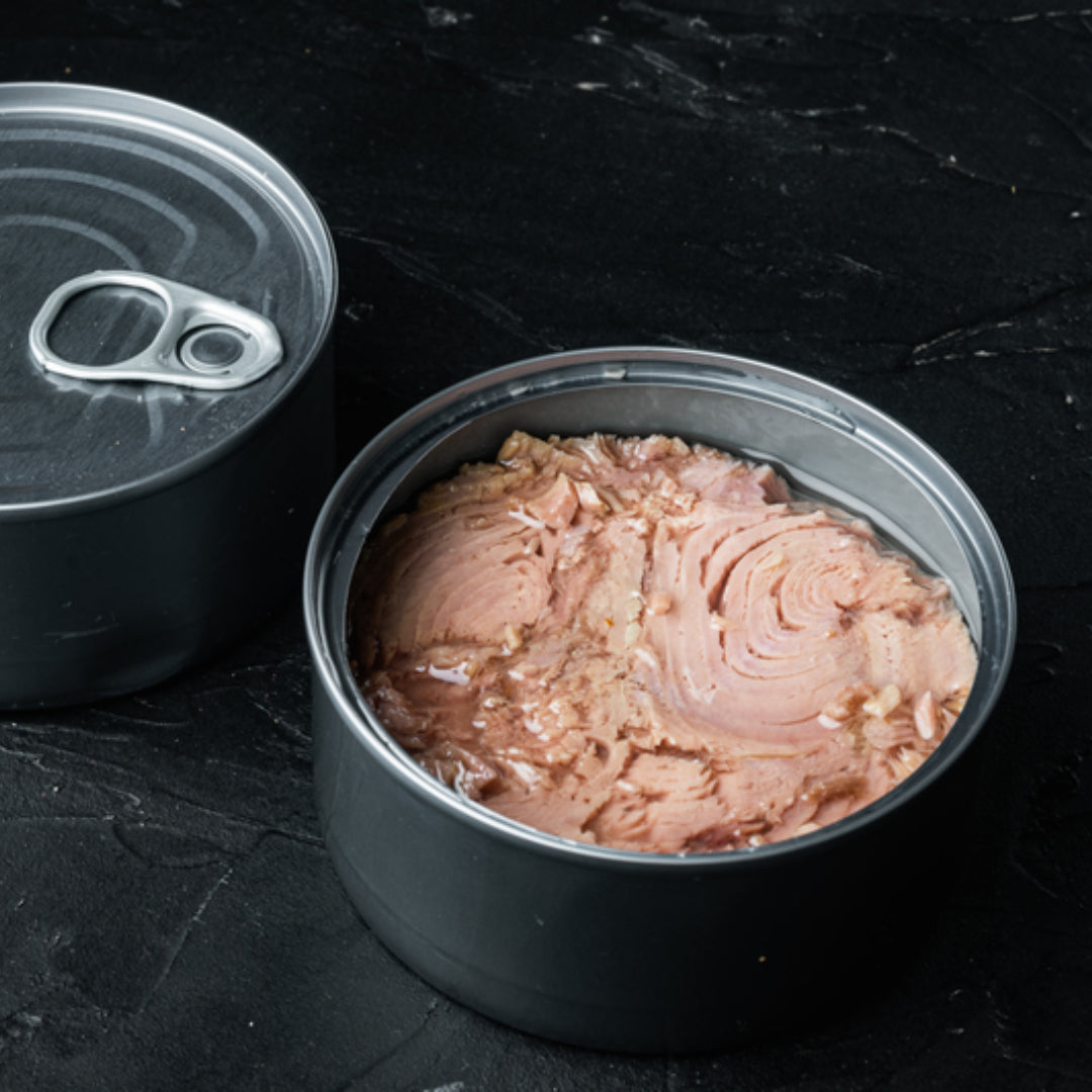 Open can of wild-caught albacore tuna with fresh herbs and lemon on a wooden cutting board