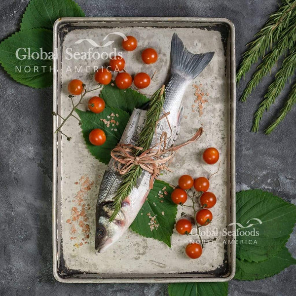 Whole Branzino fish on a metal tray, garnished with fresh cherry tomatoes for a simple and vibrant seafood presentation