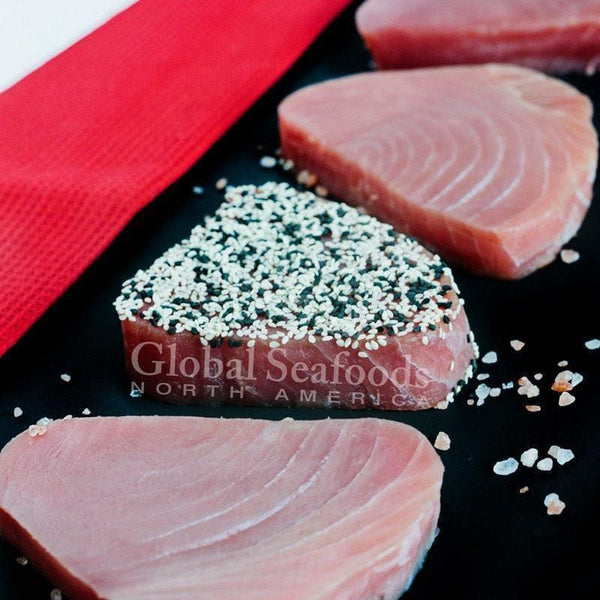 Raw tuna steaks on a black surface with coarse salt