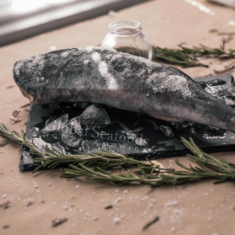 Frozen headless sablefish on a dark board with herbs.