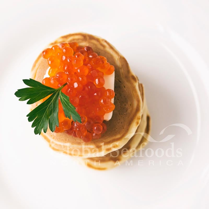 A sumptuous serving of Red Salmon Caviar in a crystal bowl, showcasing its vibrant red-orange hue and glossy, uniformly sized beads, epitomizing luxury and gourmet taste