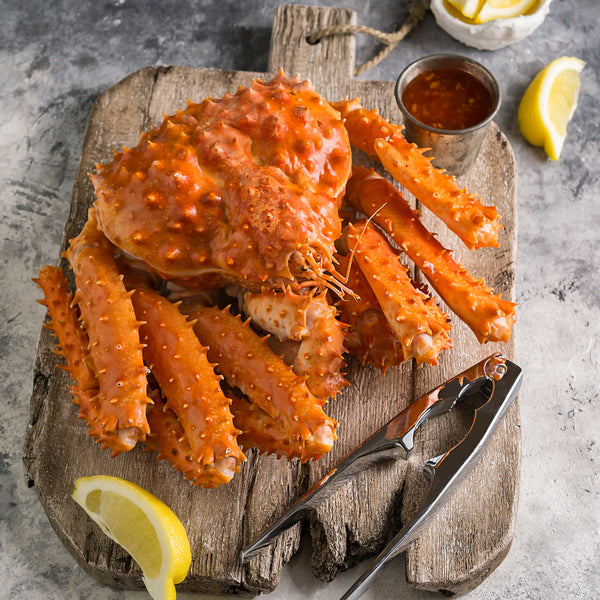 Whole cooked king crab on a wooden cutting board, served with lemon slices and a crab cracker for a classic seafood presentation