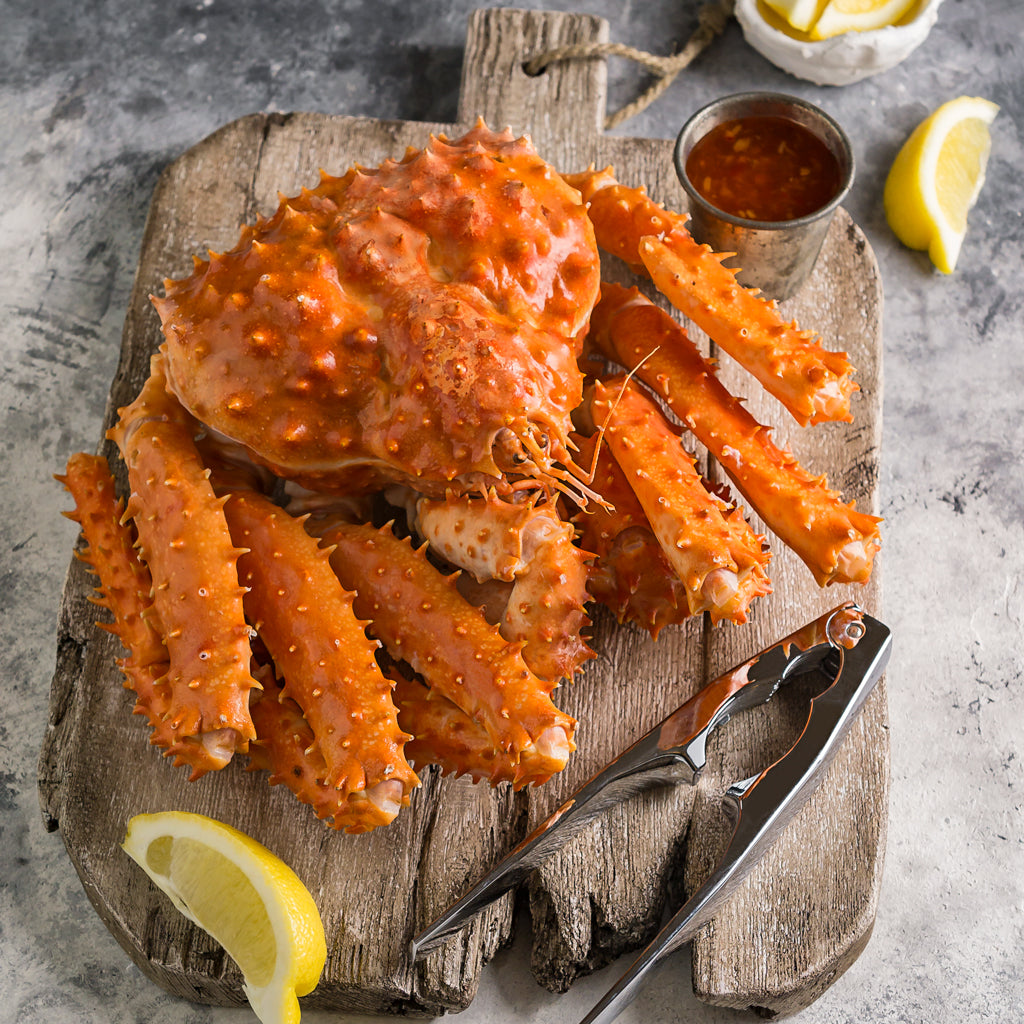 Whole cooked king crab on a wooden cutting board, served with lemon slices and a crab cracker for a classic seafood presentation