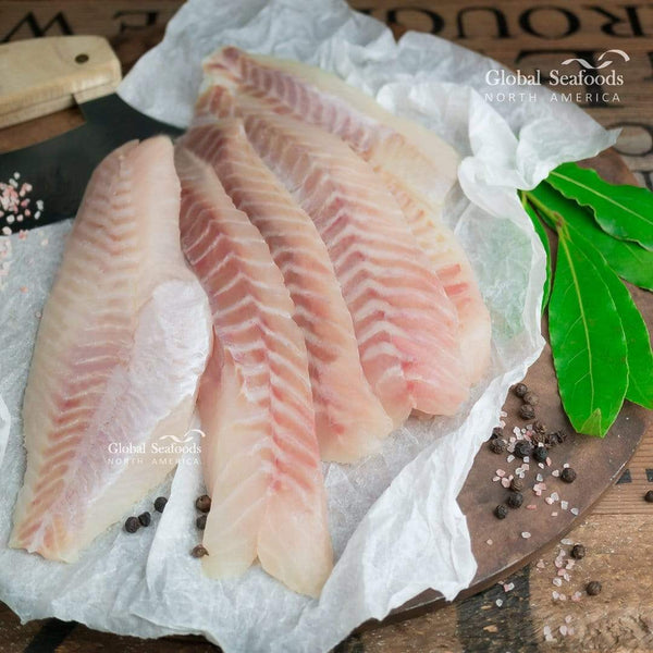 Fresh rockfish fillets placed on white paper over a wooden board, surrounded by spices for a clean and rustic seafood preparation display