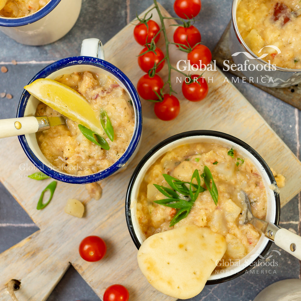Two bowls of creamy salmon chowder on a wooden cutting board, one with crackers and the other with a lemon slice, spoon inside each bowl
