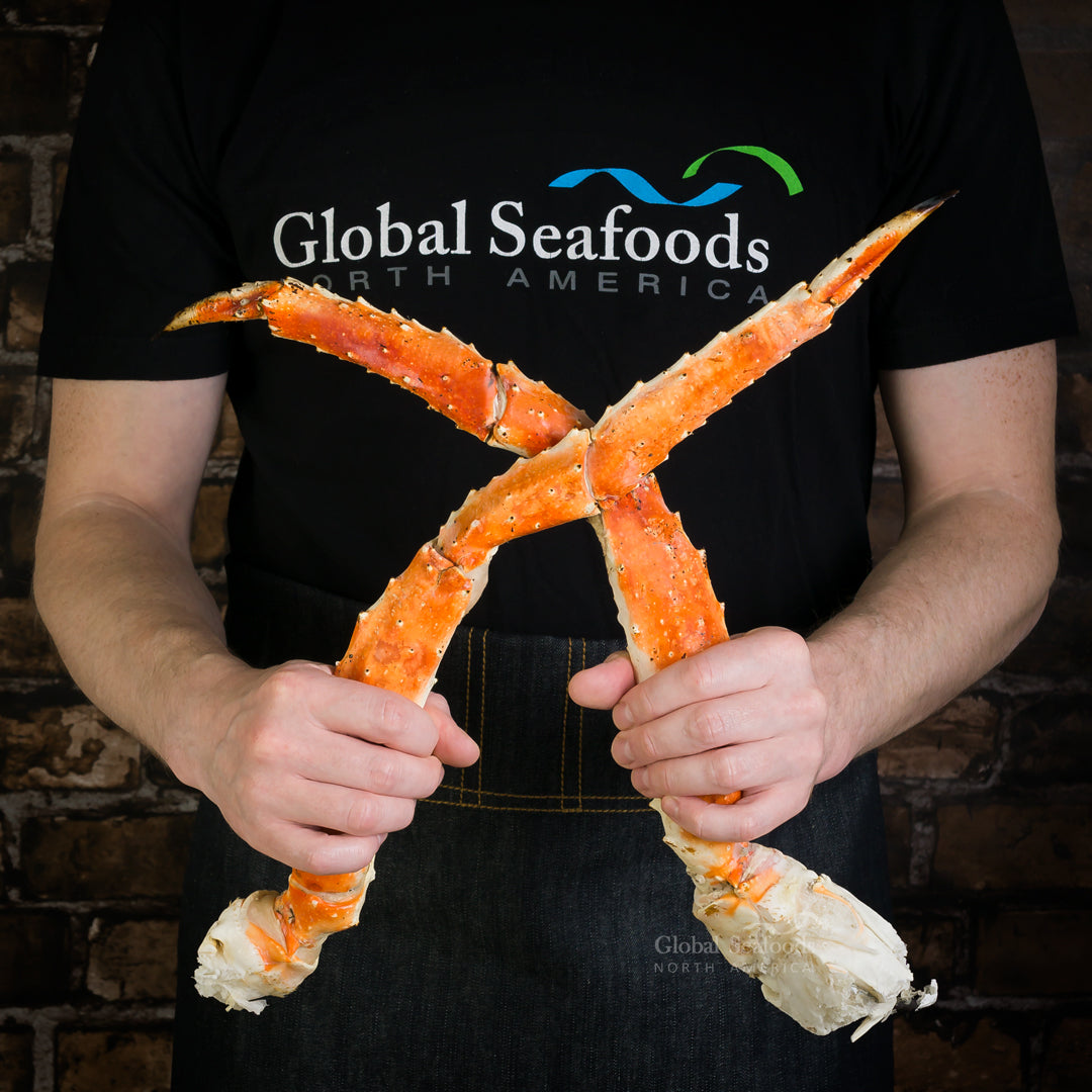 Person holding two cooked red king crab legs in front of a Global Seafoods shirt