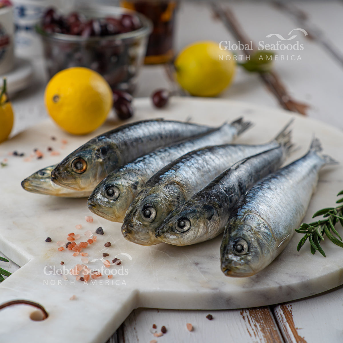 Whole sardines on a round stone board with lemon and seasonings nearby