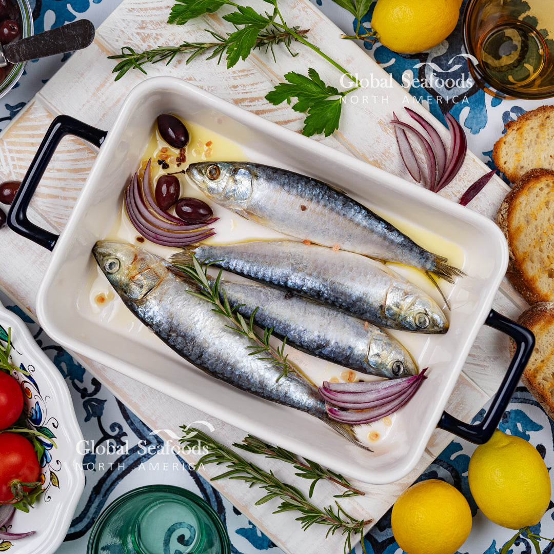 Whole sardines in a rectangular ceramic dish with red onion and herbs