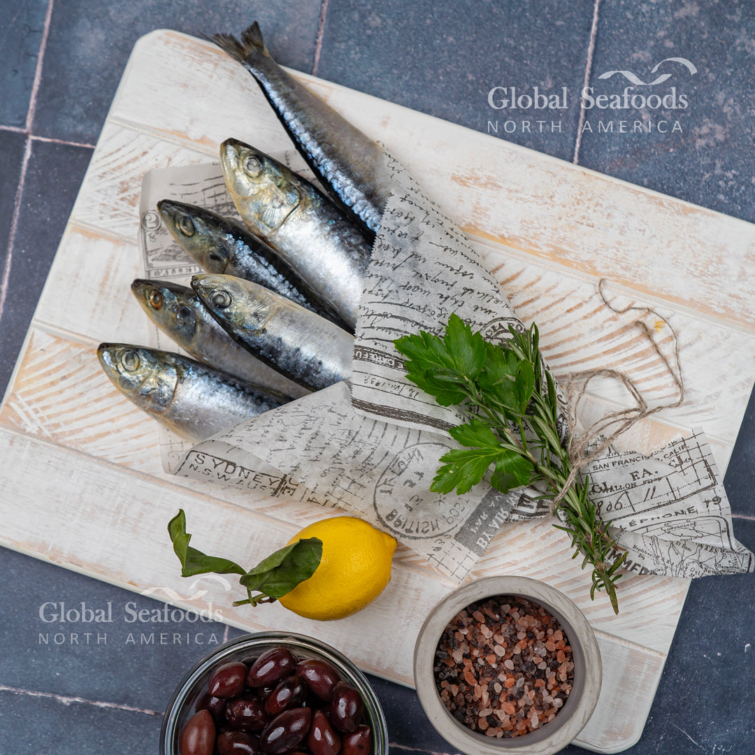 Whole sardines partially wrapped in cloth on a wooden board