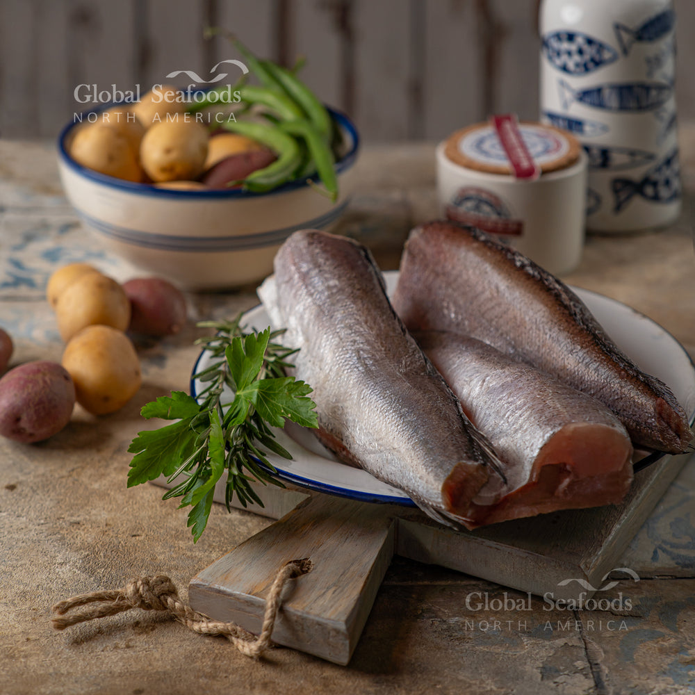 Whole Pacific whiting (hake), cleaned and trimmed without head and tail, placed on a plate with raw potatoes on a kitchen table ready for cooking