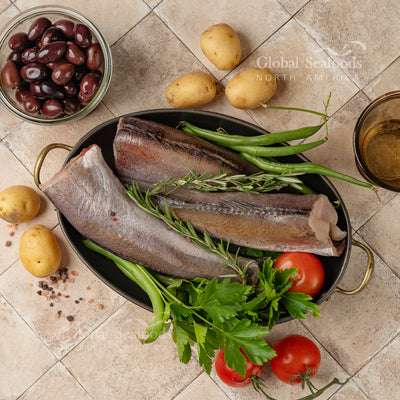 Prepared Pacific whiting fish without head and tail arranged on a plate beside potatoes, set for home-style meal preparation