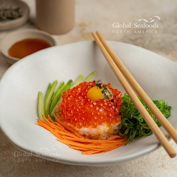 ikura (red caviar) from Coho salmon served over rice with a square piece of seaweed, presented on a plate with chopsticks on the side