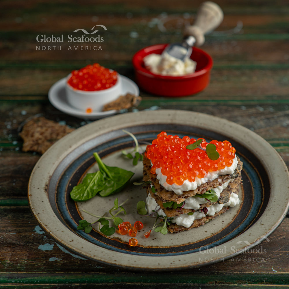 Appetizer plate with crackers topped with cream cheese and red caviar, arranged for serving

