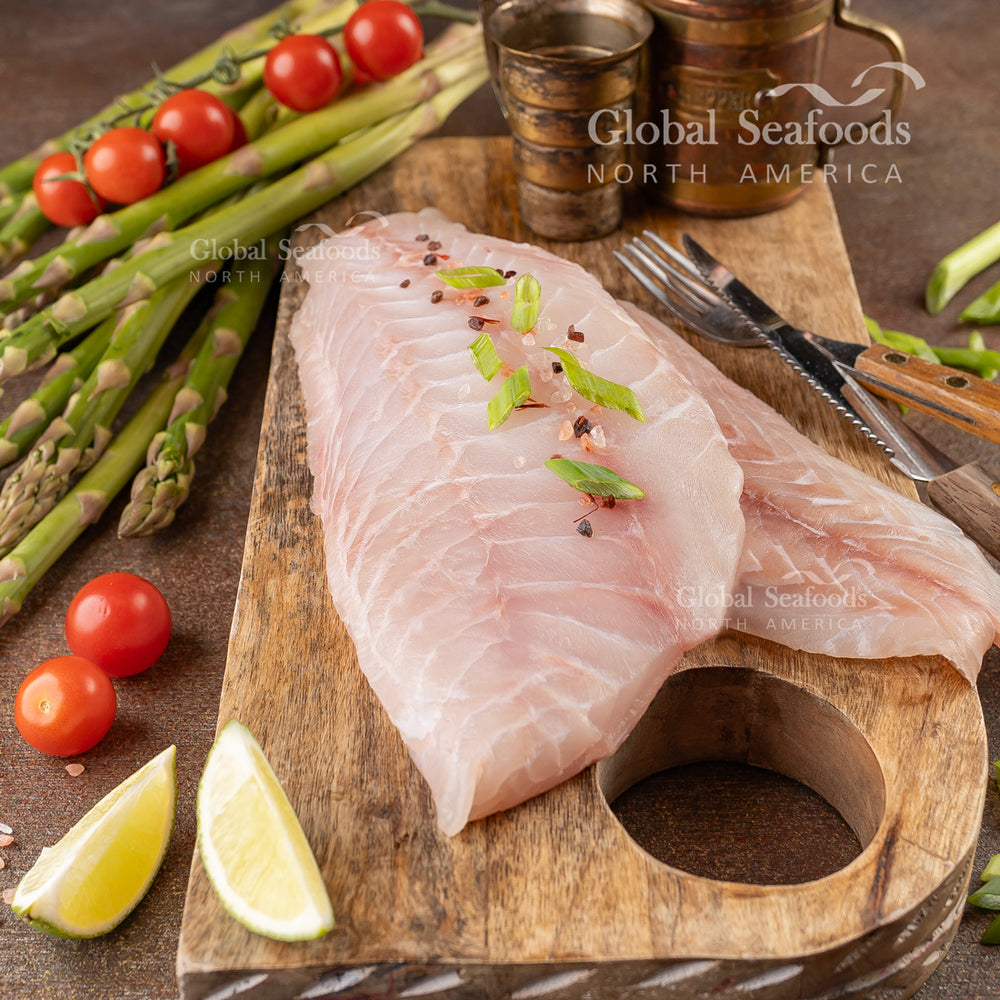 Two grouper fillets on a wooden cutting board, served with grilled asparagus and cherry tomatoes, with sliced lemon on the side for garnish.