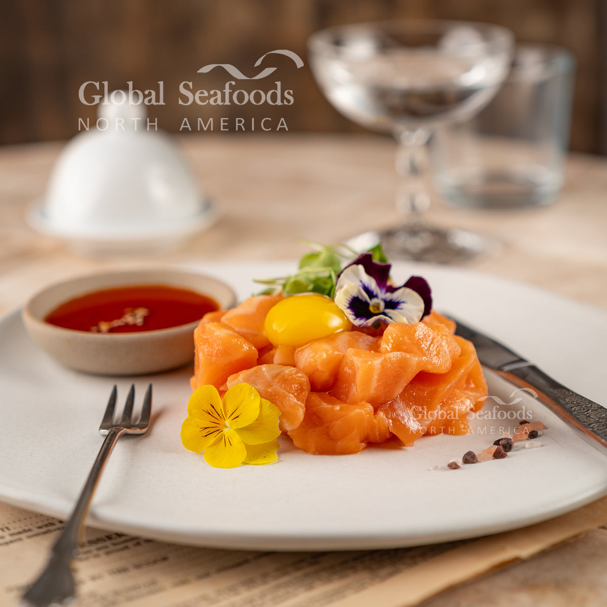 Cube-cut Atlantic salmon poke arranged on a white plate, served next to a small side dish with sauce for dipping