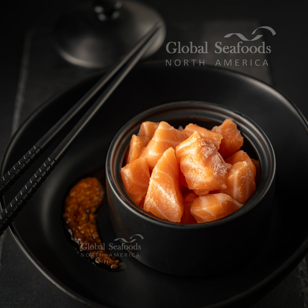 Cube-cut Atlantic salmon poke served in a small black bowl and on a black plate, topped with sauce for garnish