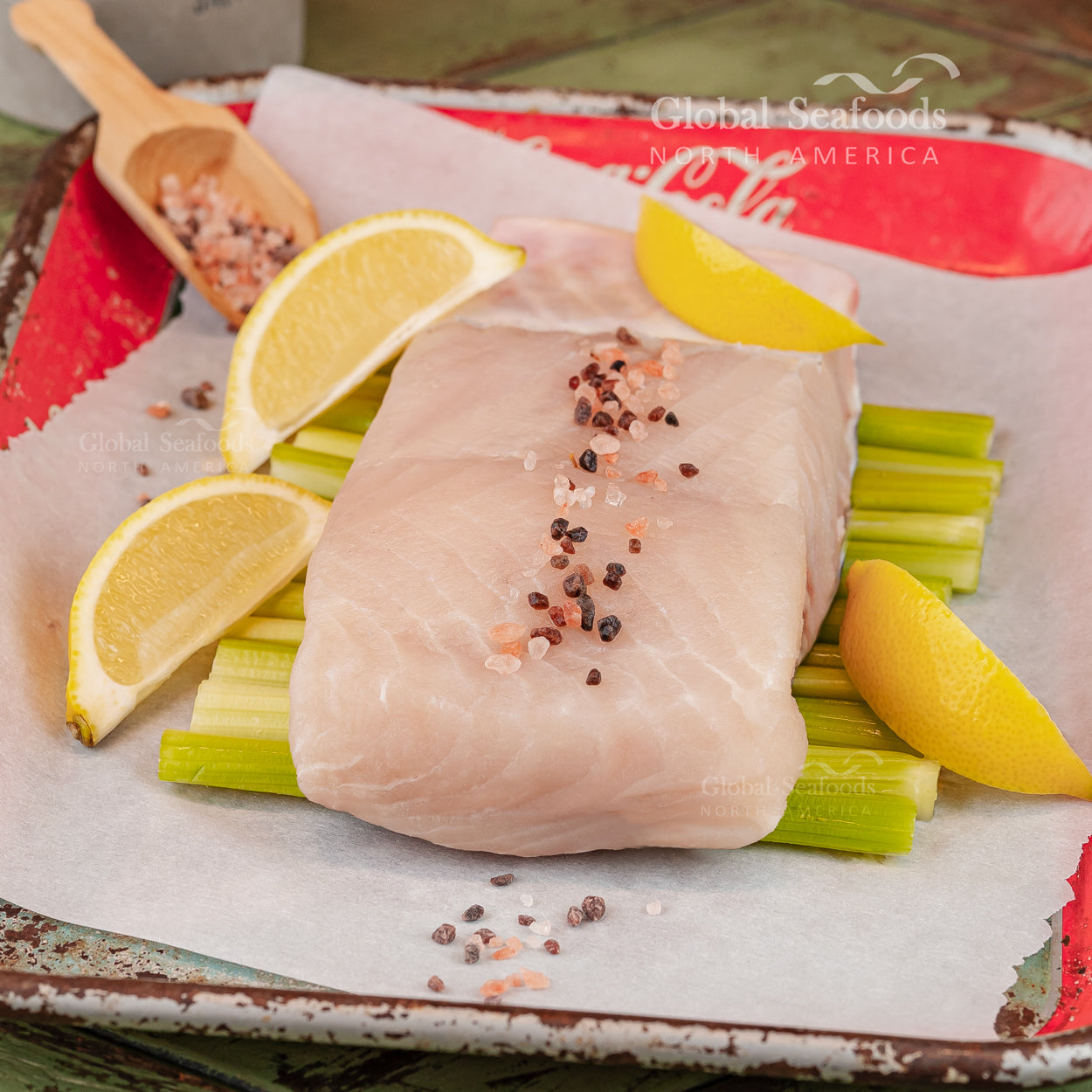 Raw sturgeon fillet with lemon wedges and celery on a tray, seasoned with spices, branded 'Global Seafoods'.