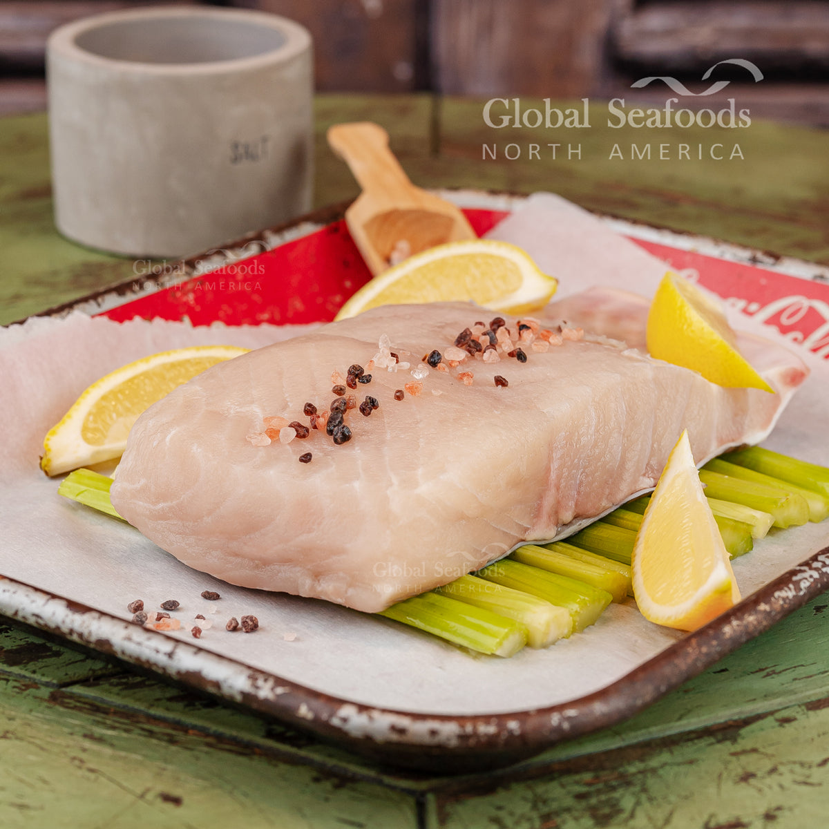 Raw sturgeon fish fillet on a plate with lemon wedges and celery, branded 'Global Seafoods North America'.
