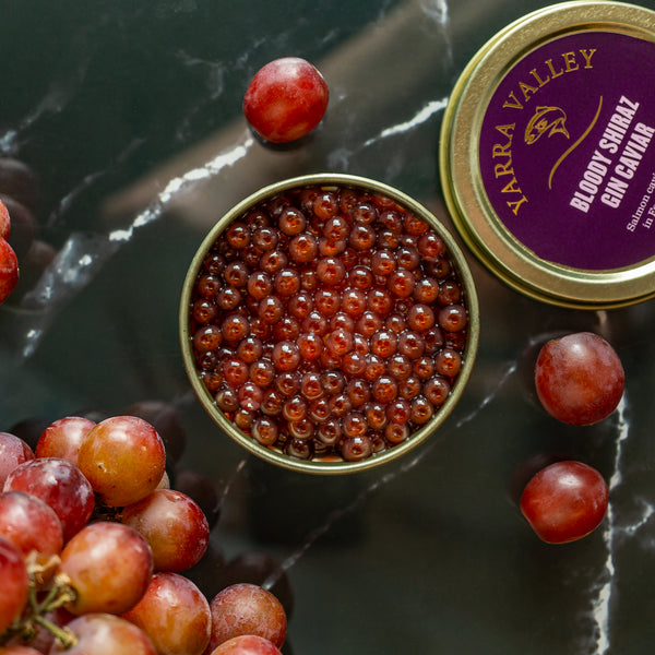 Open tin of Bloody Shiraz infused caviar on a dark surface, paired with fresh grapes for a rich and luxurious visual