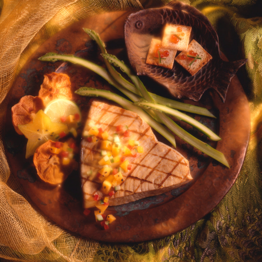 Hot smoked wild-caught swordfish slices served on a wooden dish alongside fresh asparagus, ready for gourmet presentation