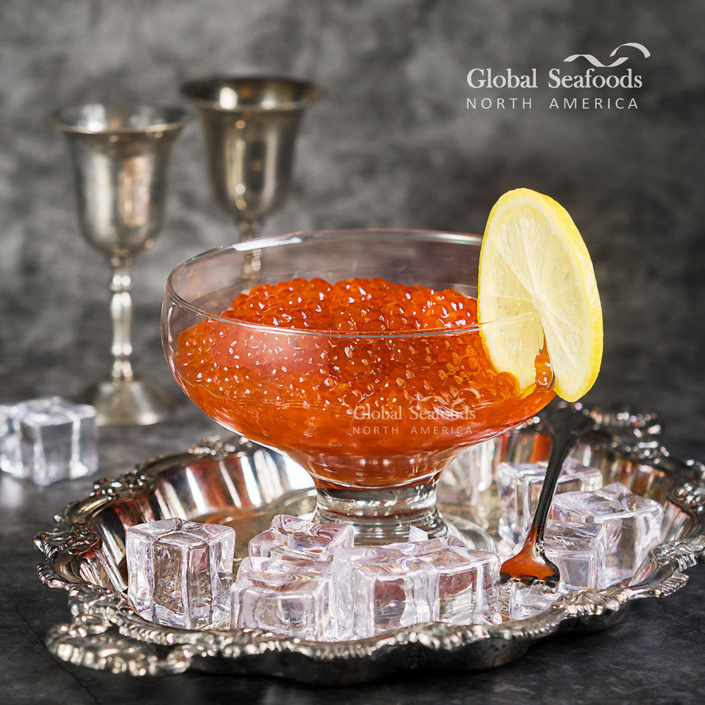 Elegant serving of red salmon roe in a glass bowl on silverware, accompanied by silver drinking cups behind for a refined presentation