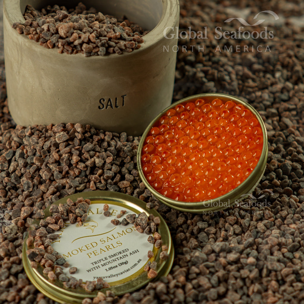 Open tin of smoked salmon caviar beside its lid and a container marked Salt, surrounded by coarse brown salt