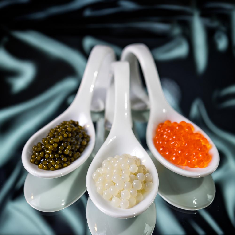 Dark caviar, white roe and salmon roe served in three white ceramic spoons