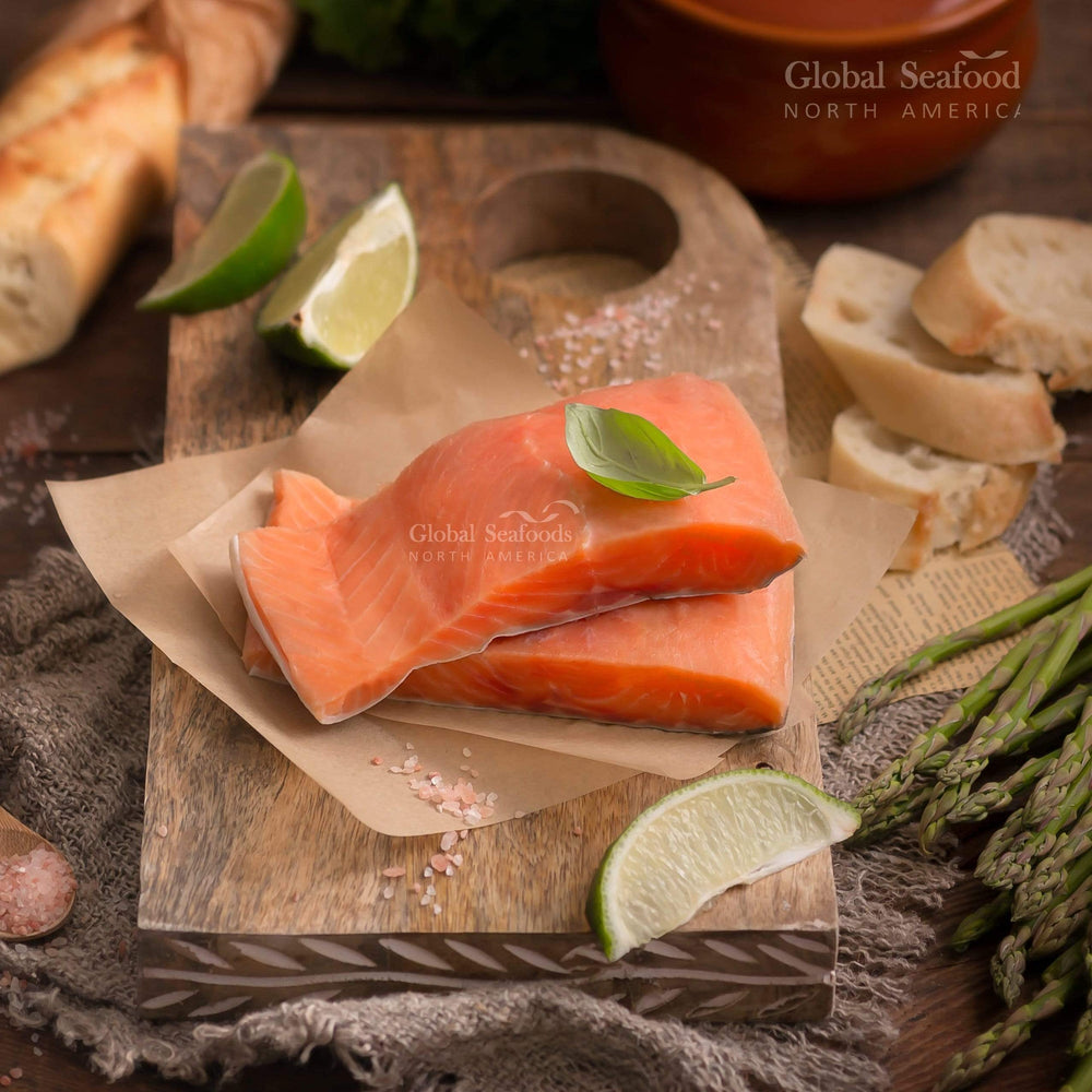 Two chum salmon fillet portions stacked on parchment with lime and asparagus nearby