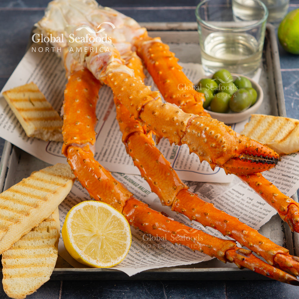 Fresh Golden King Crab legs displayed on a silver tray with crisp toasts, lemon wedges, and a cup of green olives, ready for serving