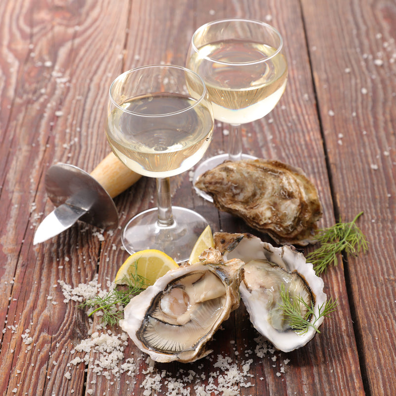 Oysters on a wooden table with an oyster knife and wine glasses