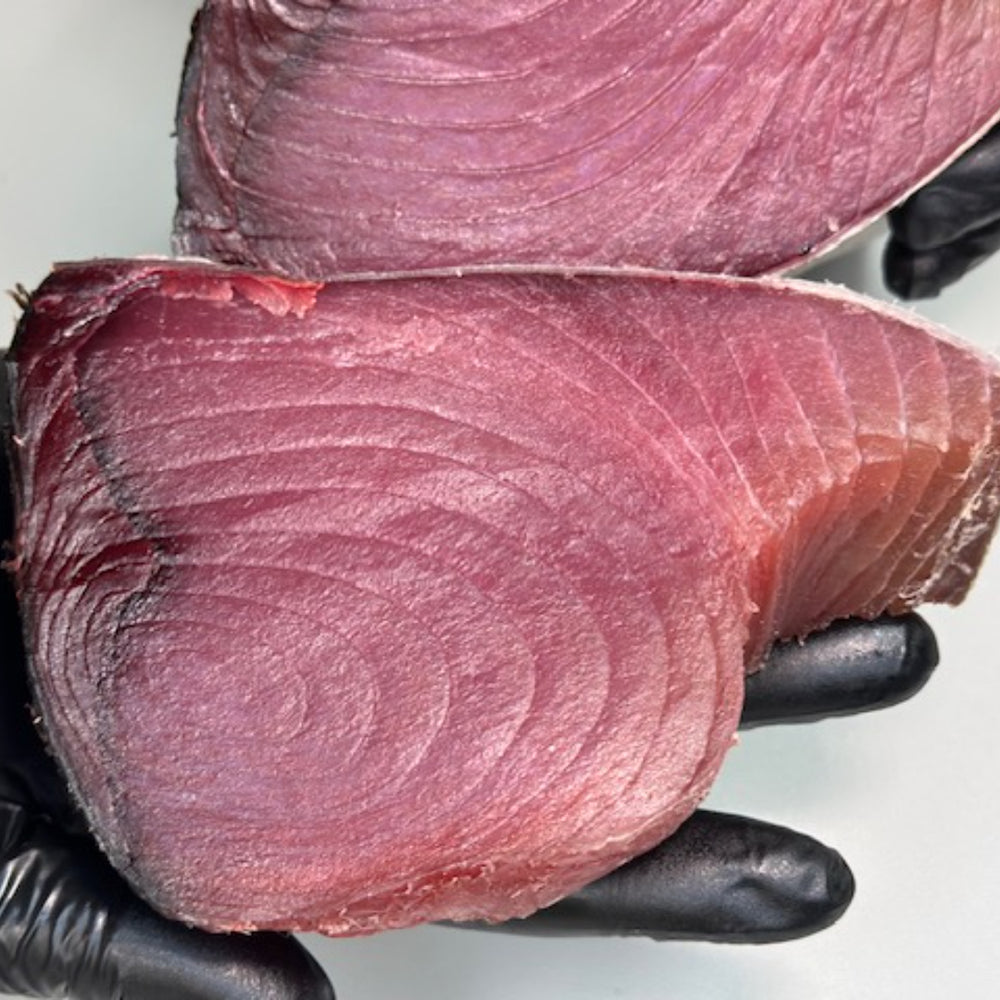 Two dry-aged yellowfin tuna steaks held in hands, showing firm texture and deep color from the aging process