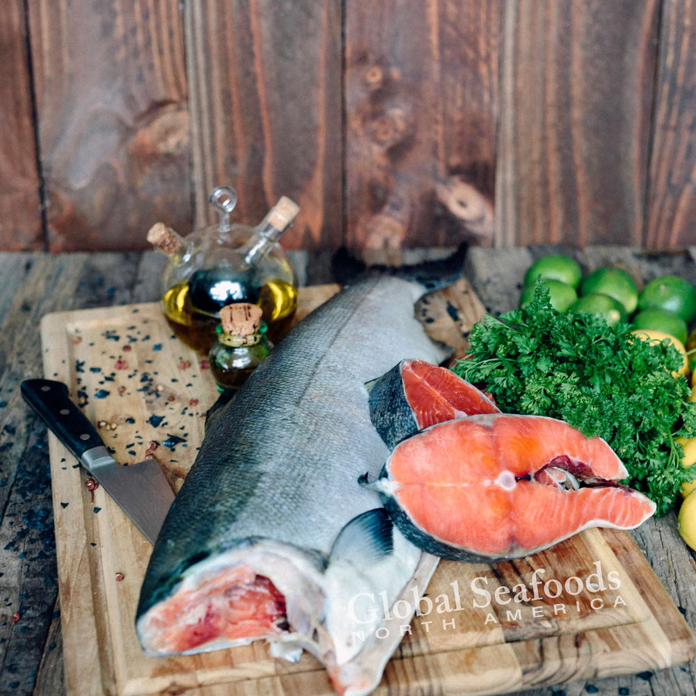 Whole king salmon without head and two cut steaks displayed on a wooden cutting board, showcasing rich red flesh and premium freshness