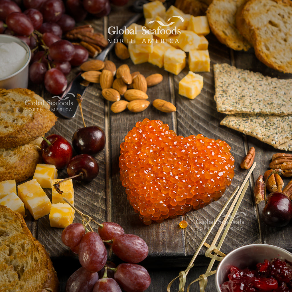 Washington rainbow trout roe arranged in a heart shape on a wooden board with cheese, grapes, cherries, nuts and crackers