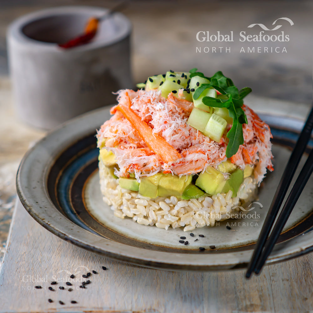 Snow crab meat served on a bed of rice, topped with sliced avocado and diced cucumber, arranged on a plate for a fresh and vibrant seafood dish