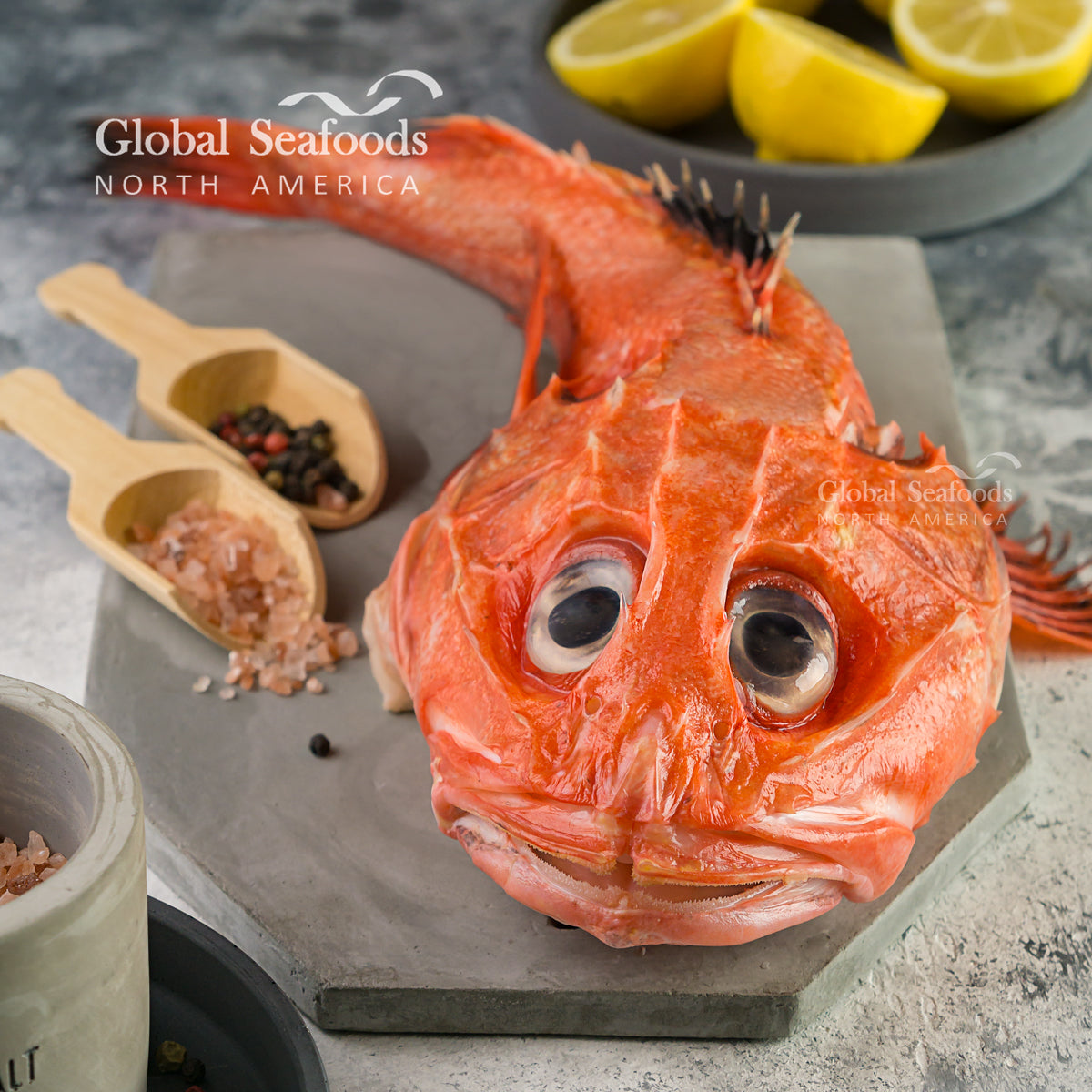 Whole kinki rockfish on a stone slab with seasonings and lemon nearby