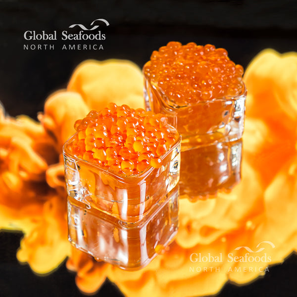King salmon caviar (ikura) served in square cups with a warm fire in the background, creating a luxurious and cozy gourmet atmosphere