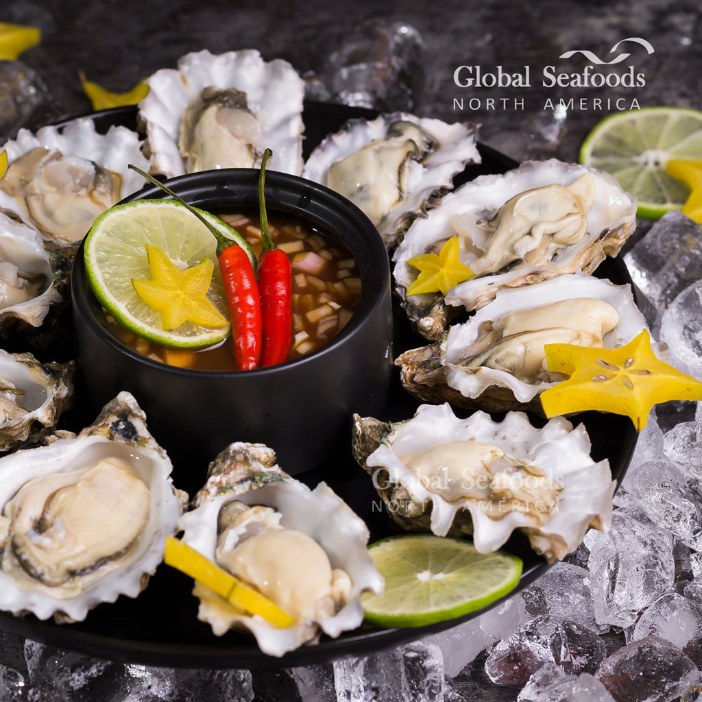 Oysters on a black plate around a cup of chili sauce
