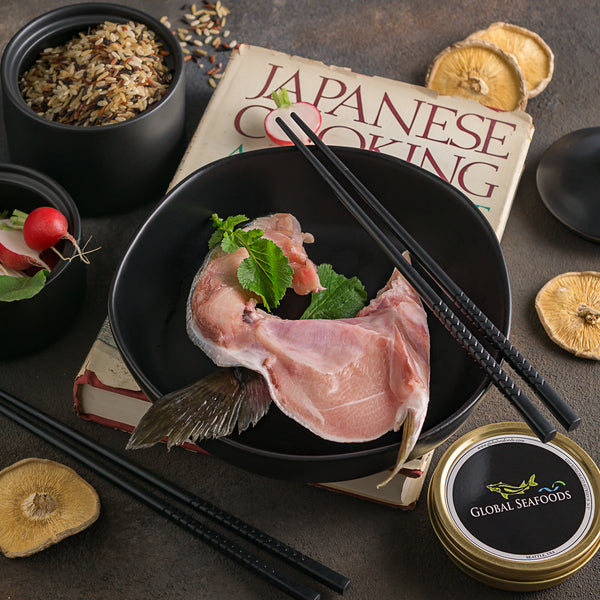 Hamachi (yellowtail) collar on a black plate with chopsticks and a tin of black caviar