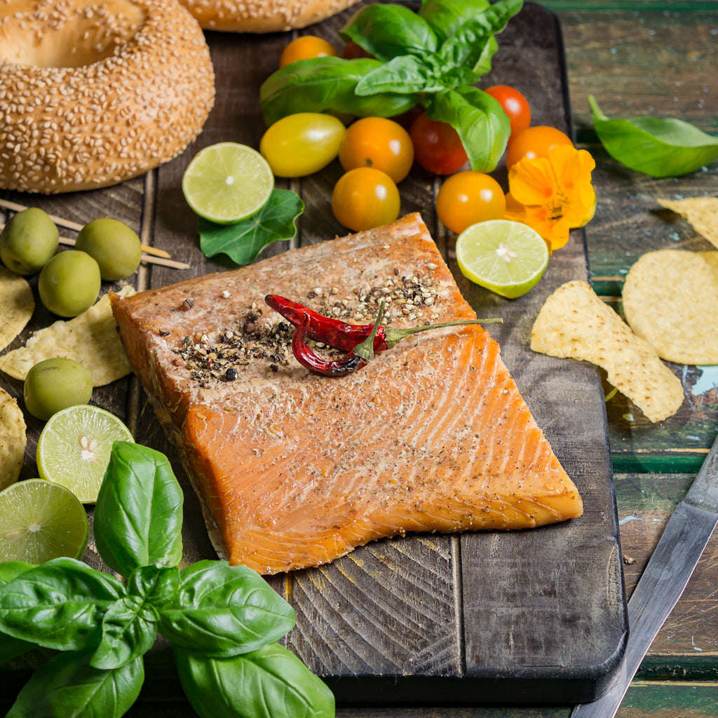 Hot-smoked Alaskan king salmon on a wooden board, served with a bagel, cherry tomatoes, lime wedges, and olives for a colorful gourmet presentation