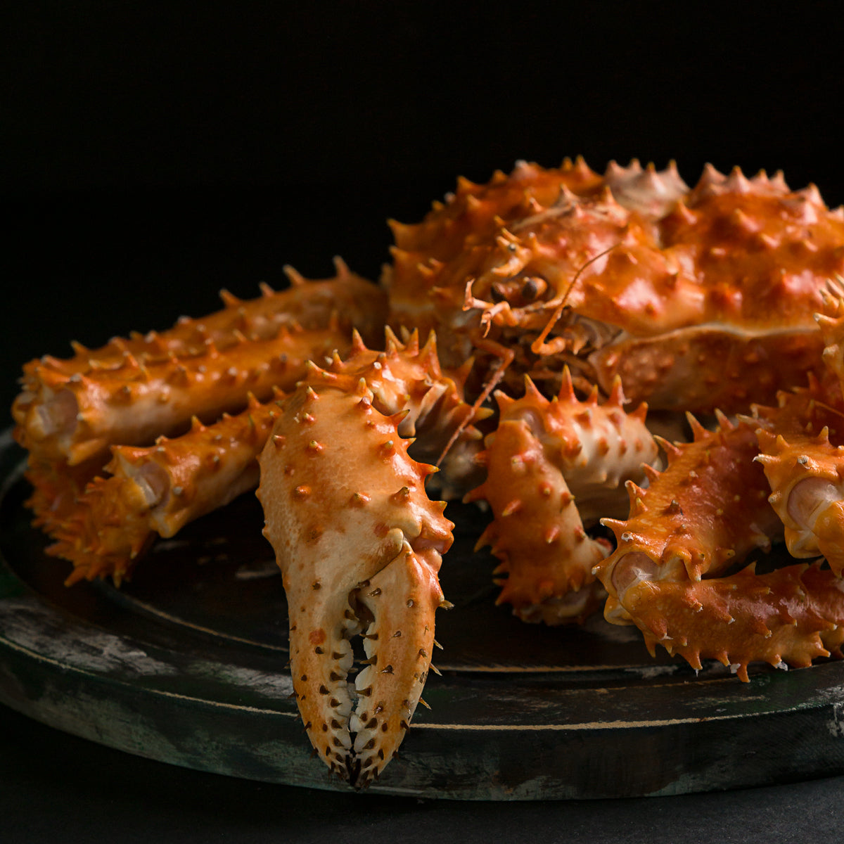 Close-up of a whole cooked king crab on a dark platter, with a large claw in the foreground